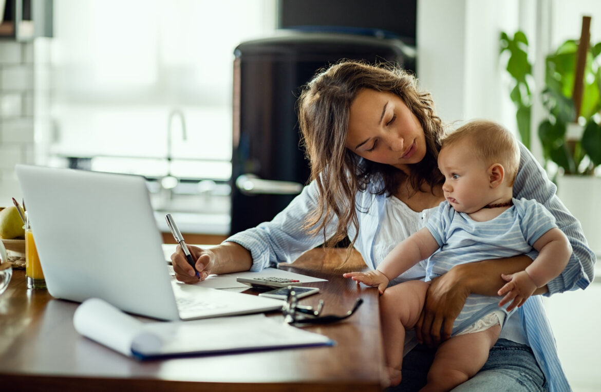 Young mother working on home finances and talking to her baby son.